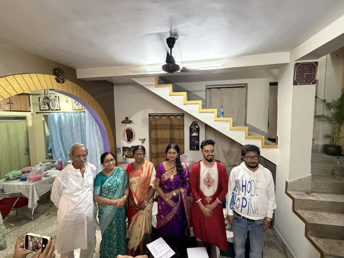 Family group photo with Babai, Ma, KumKum Ma, Rituparna, and Shoumo by the staircase