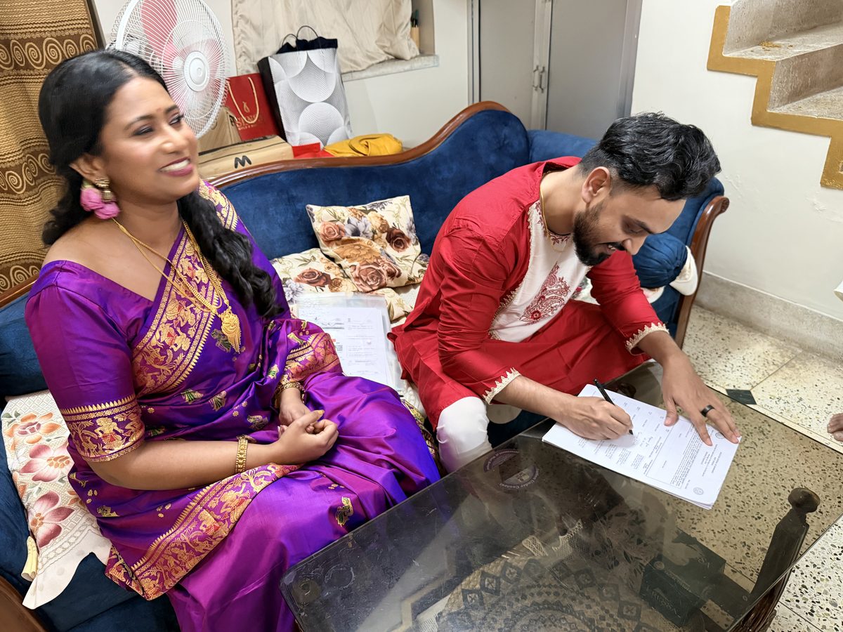 Shoumo signing documents on the couch with Rituparna beside him