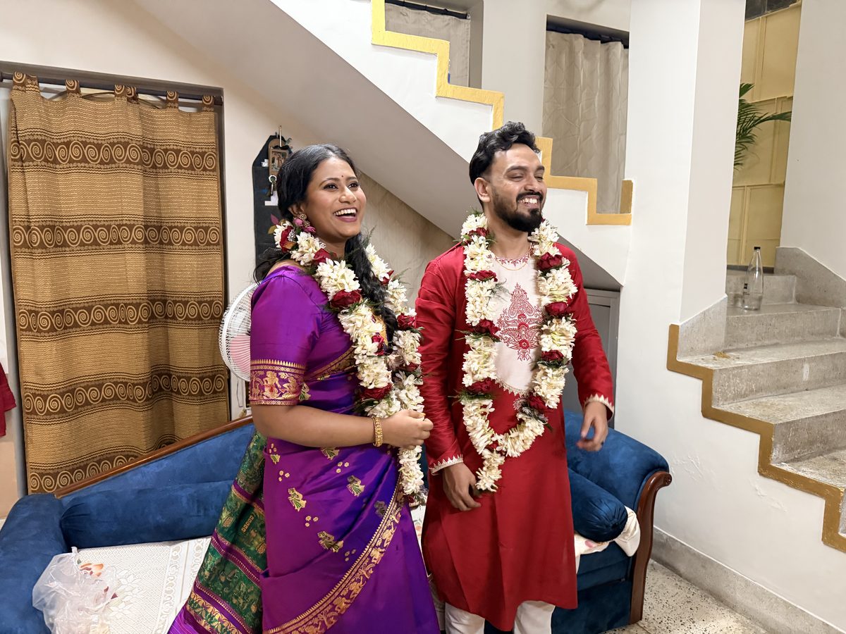 Rituparna and Shoumo laughing together with garlands by the staircase