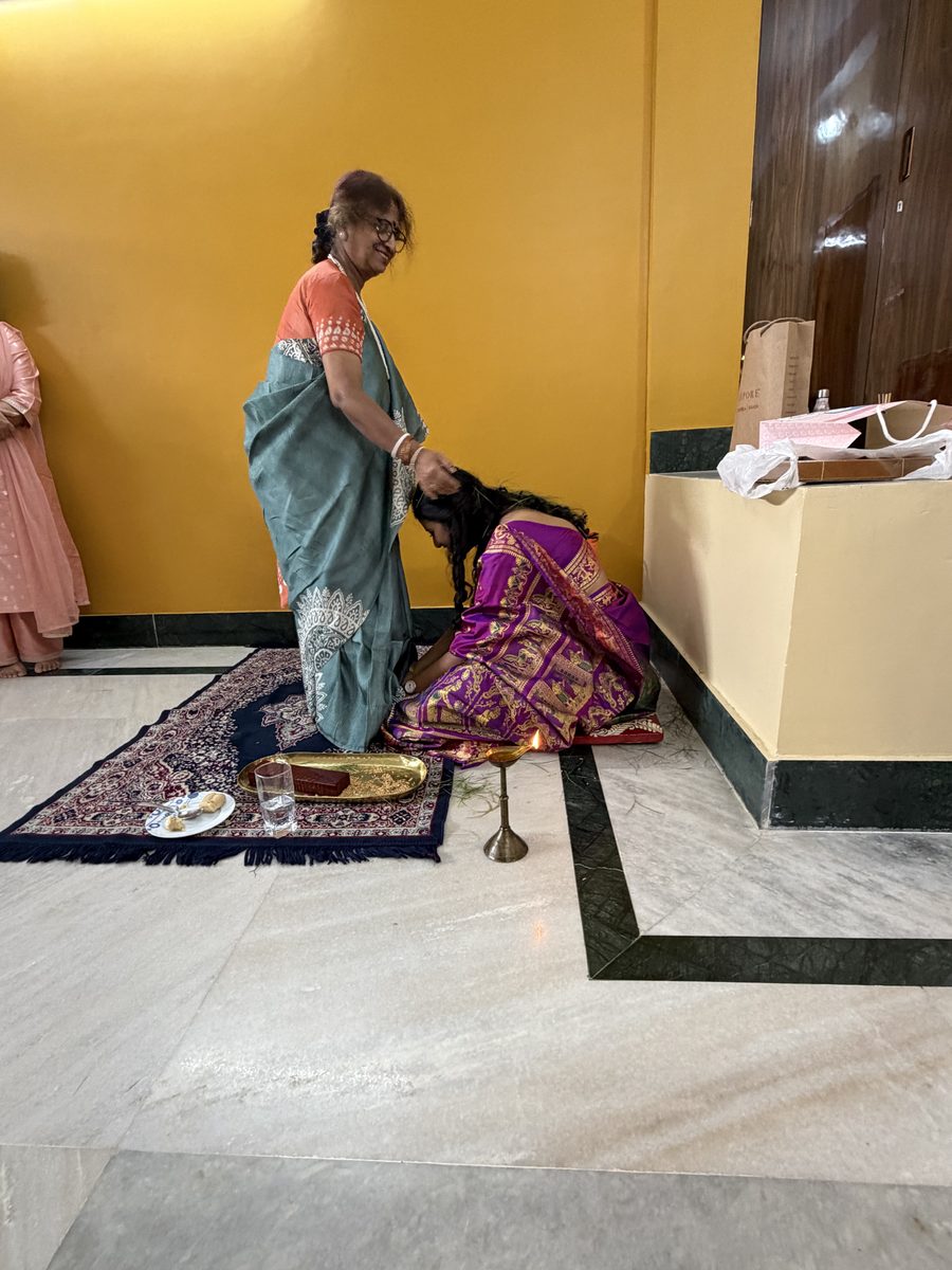 Rituparna bowing at an elder woman's feet on the prayer mat during ashirwad