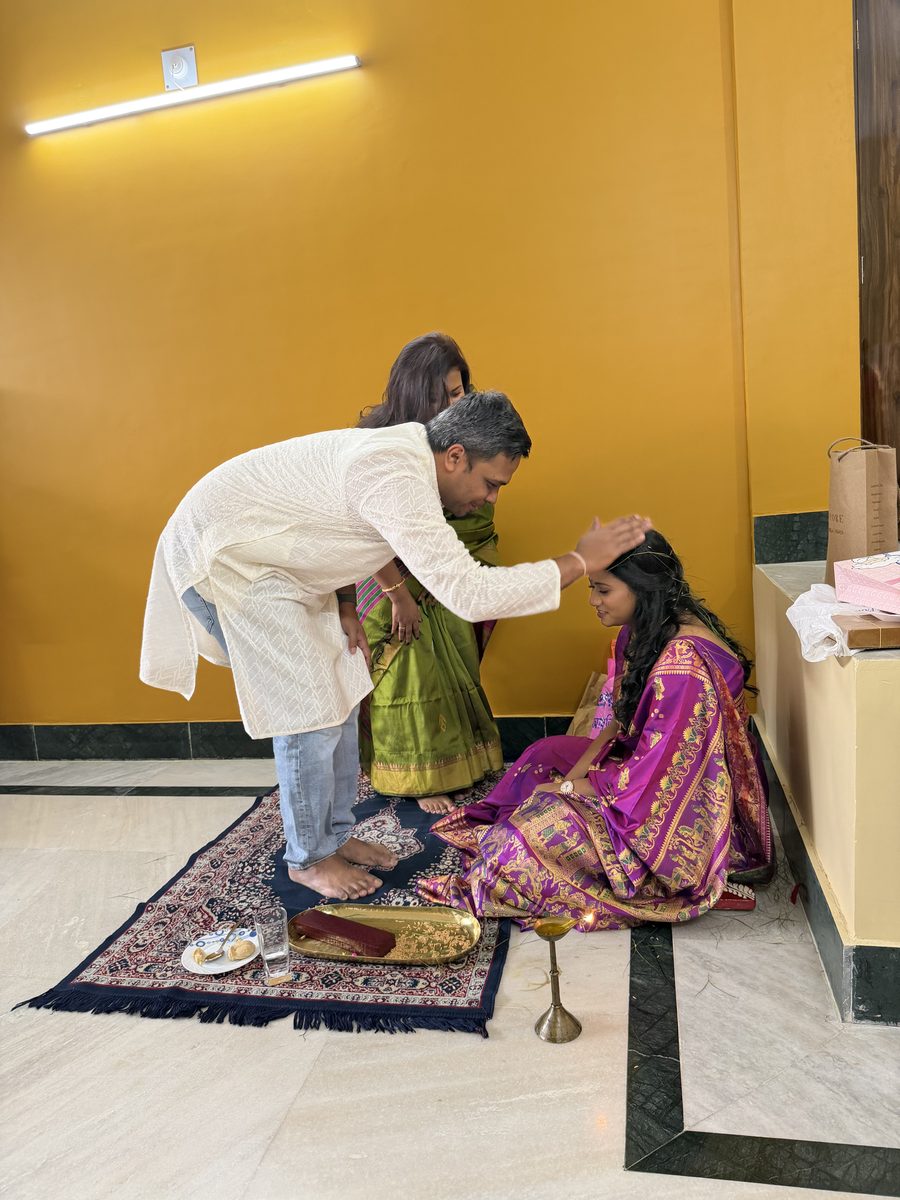 Grandfather in white blessing Rituparna seated on the prayer mat