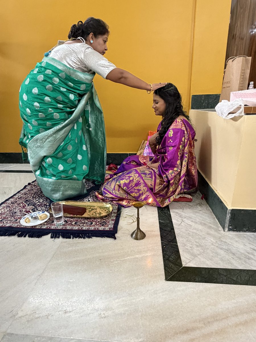 Woman in green sari blessing Rituparna in purple on the prayer mat