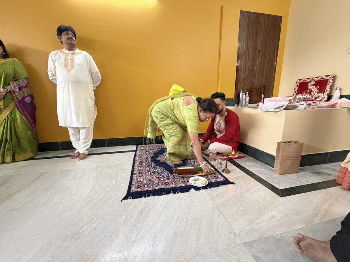 Man in green bending to receive blessings with family watching