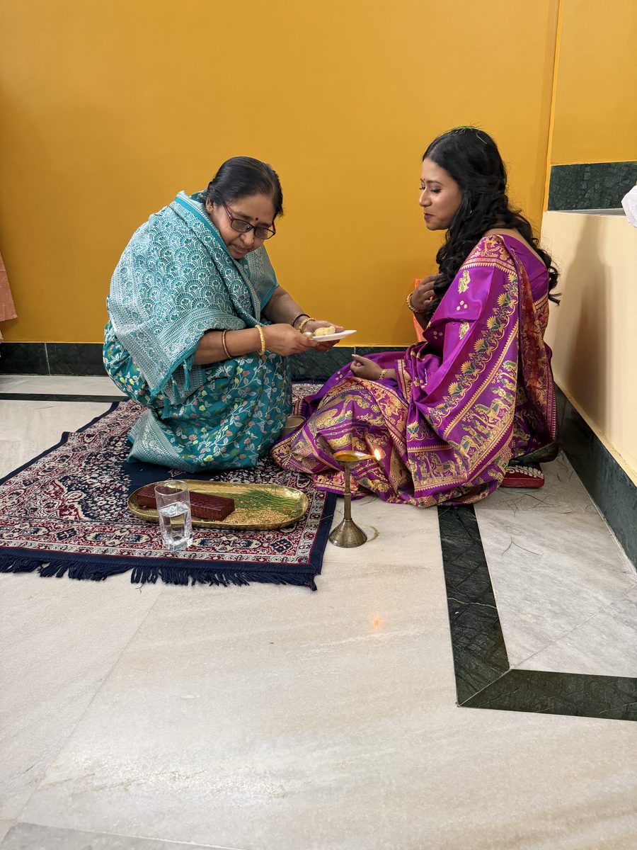 Elderly woman in turquoise sari blessing Rituparna on the prayer mat