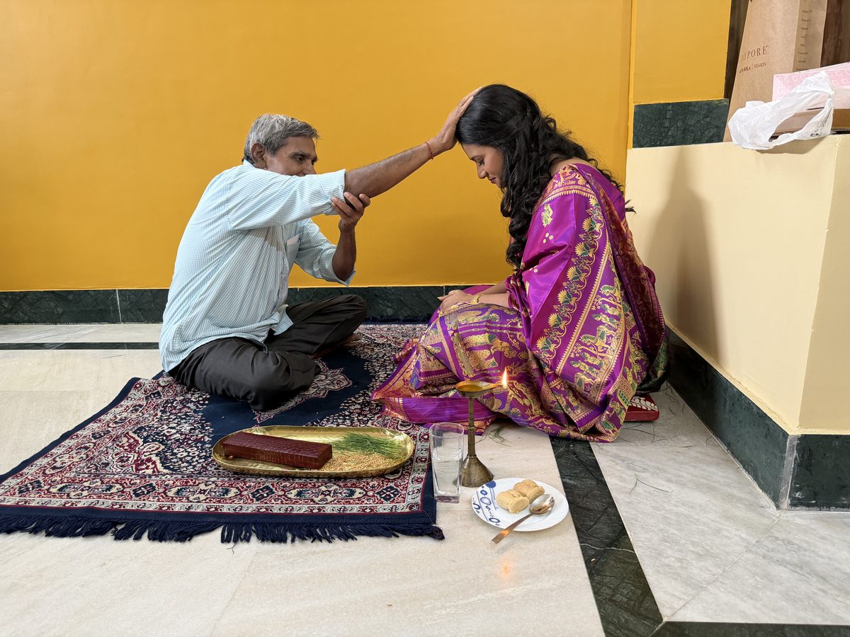 Elder man placing hand on Rituparna's head in blessing on the prayer mat