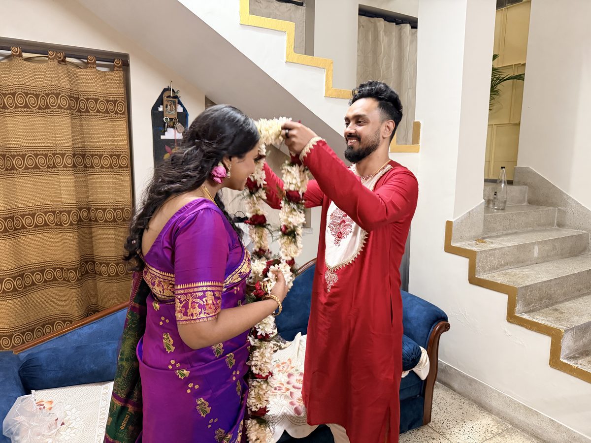 Rituparna and Shoumo exchanging flower garlands with an elder woman assisting