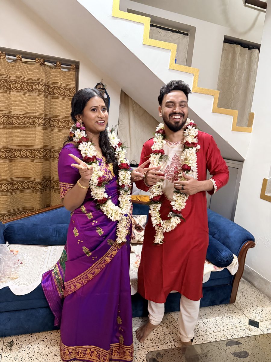 Rituparna and Shoumo holding flower garlands together, smiling indoors