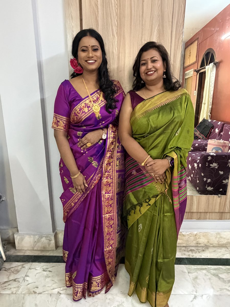 Two women in purple and green saris smiling at the camera