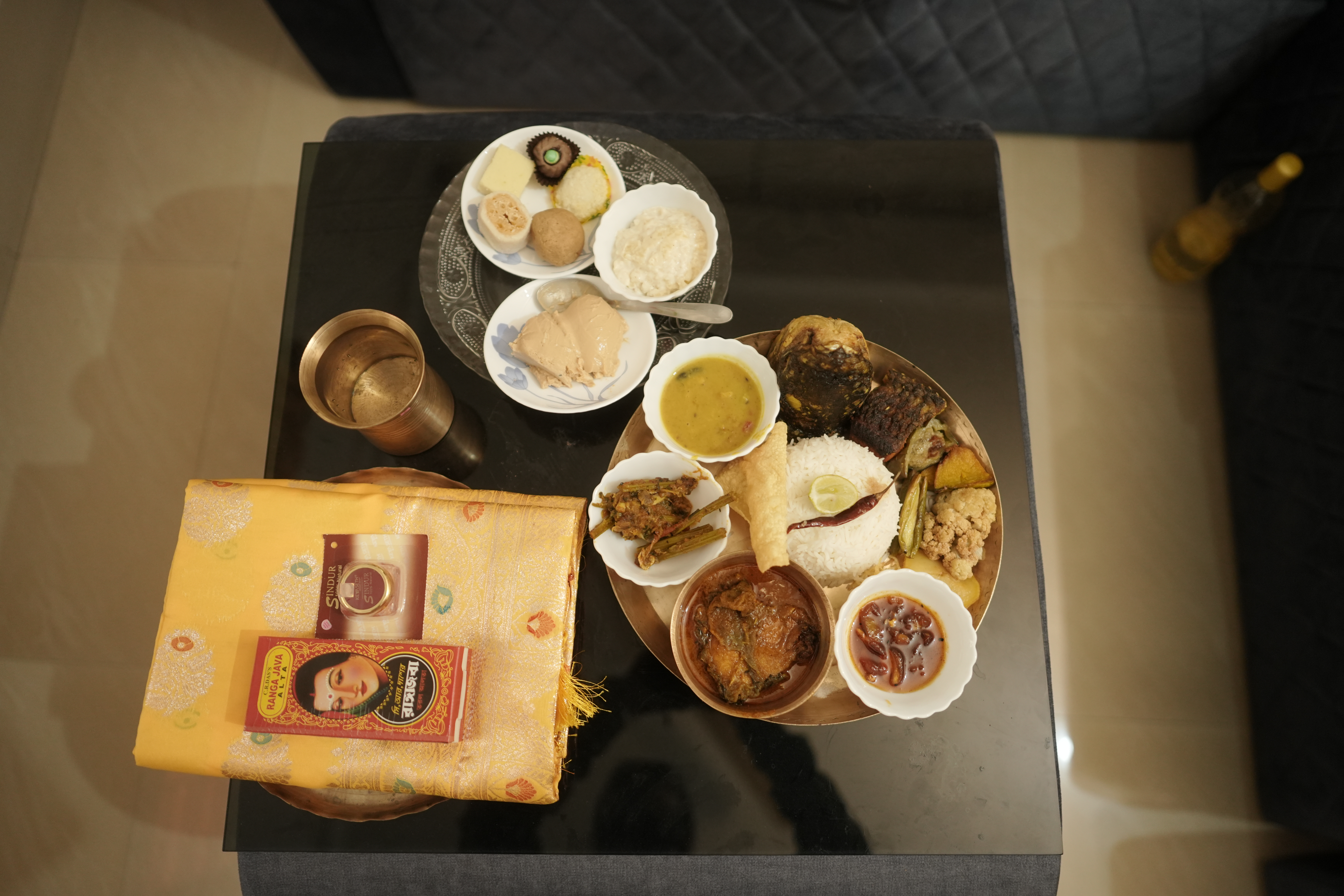 Traditional Bengali thali with rice, dal, fish, sweets and a folded sari — the bhaath-kapod offering