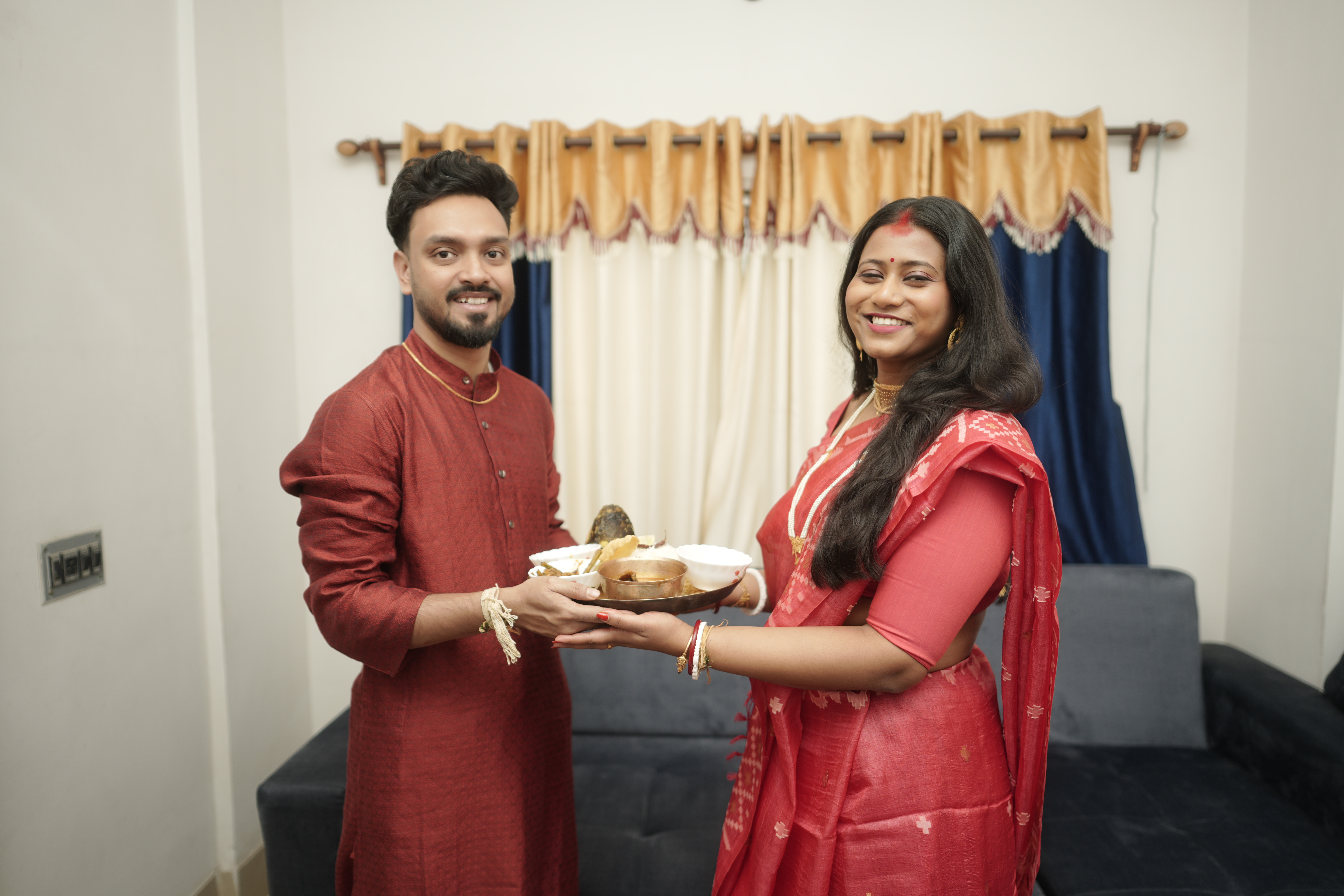 Rituparna and Shoumo smiling together, holding the ceremonial plate of sweets
