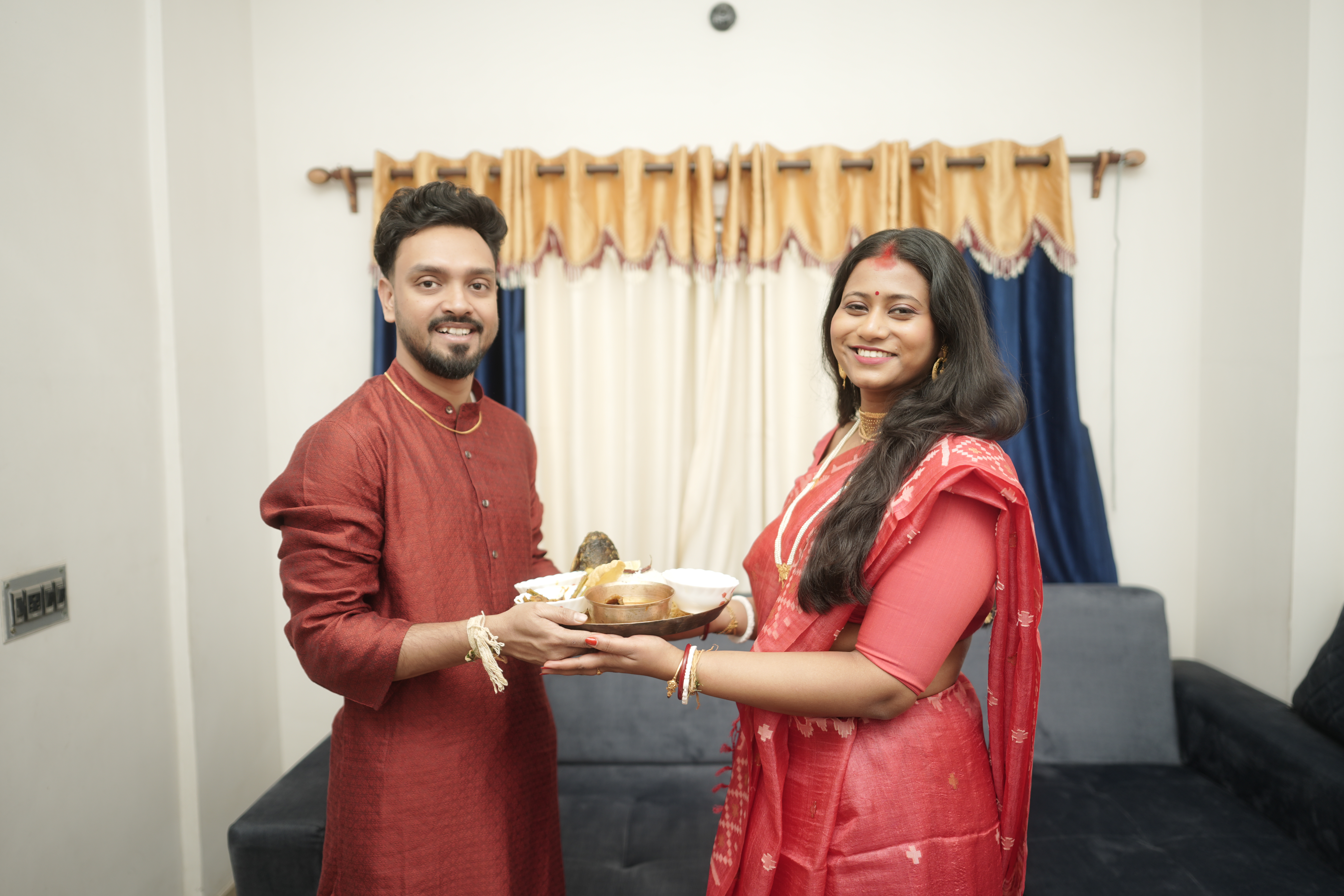 Rituparna and Shoumo posing with the ceremonial plate, radiant in red
