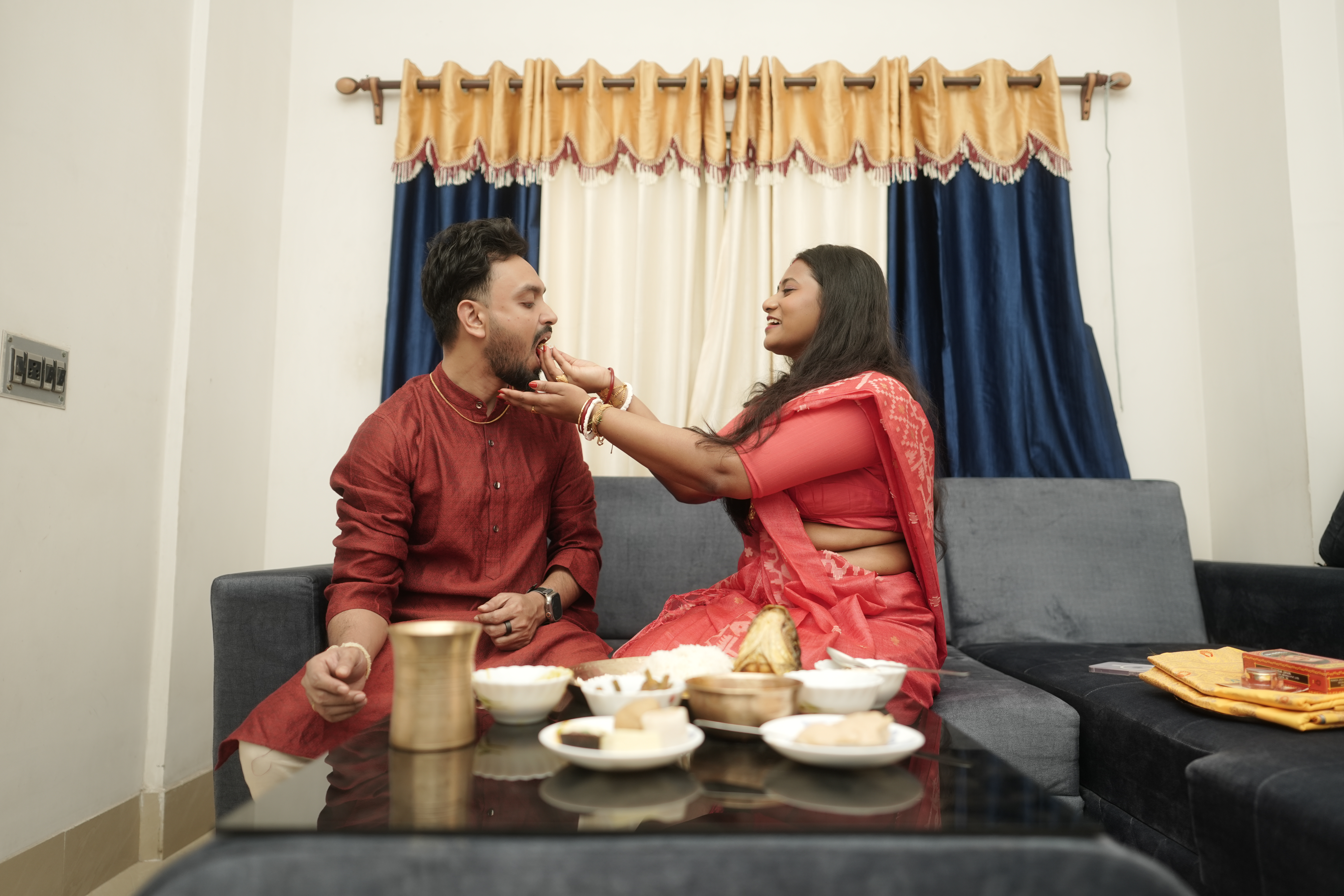 Rituparna lovingly feeding Shoumo a sweet morsel as they sit together on the couch
