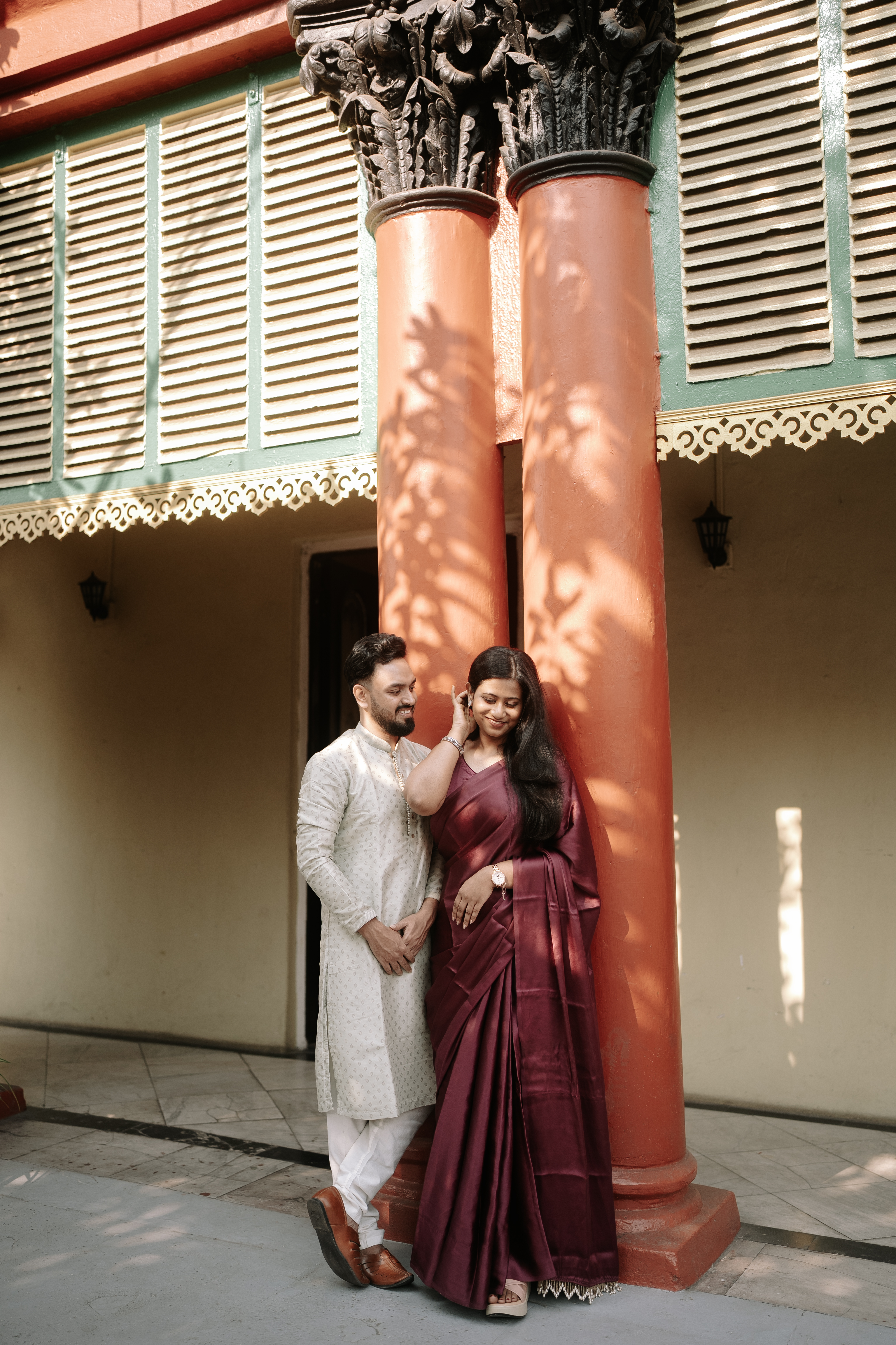 Rituparna by an exterior column, tucking her hair with a gentle gesture