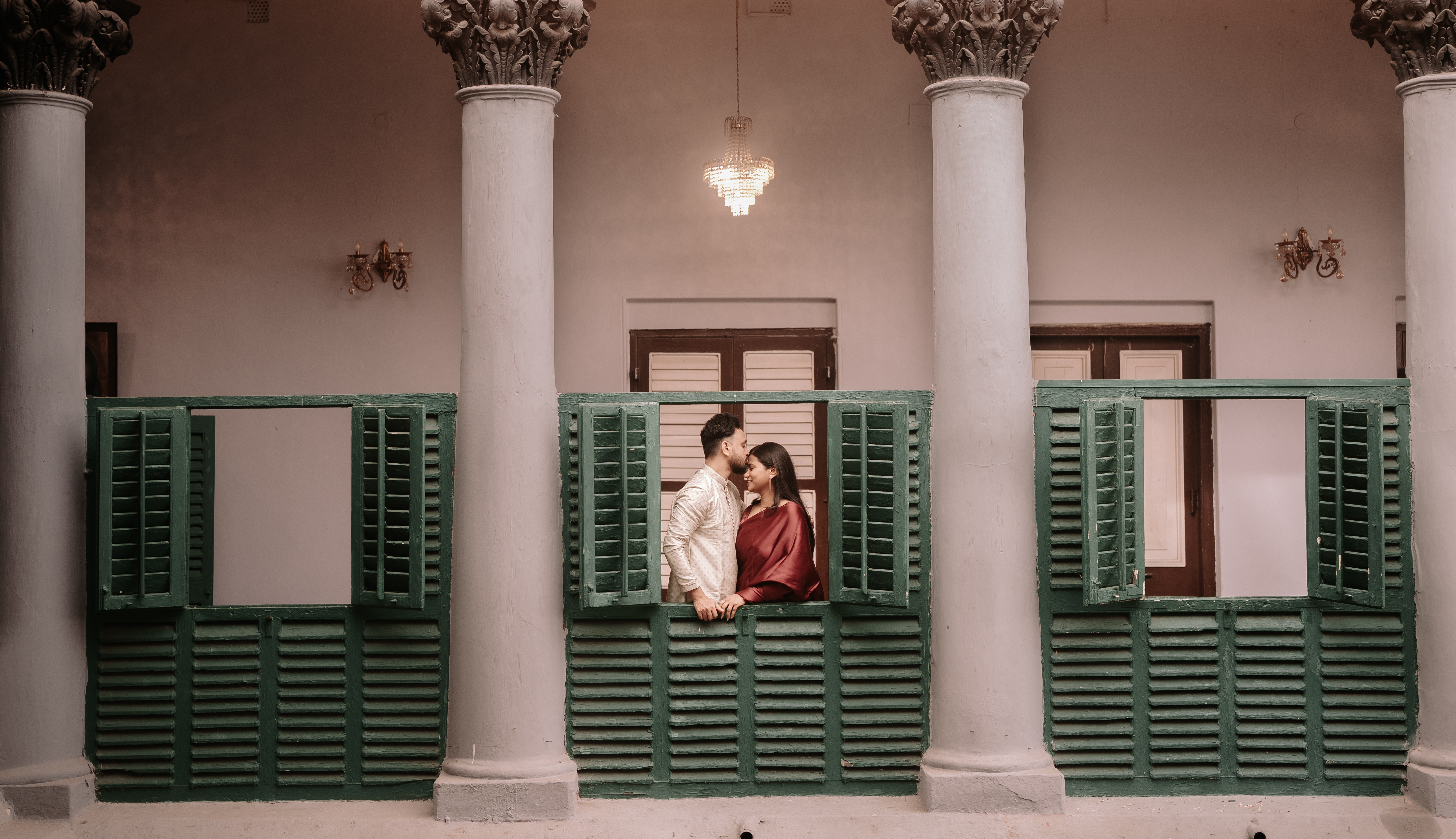 Wide shot of Rituparna and Shoumo kissing before the haveli facade