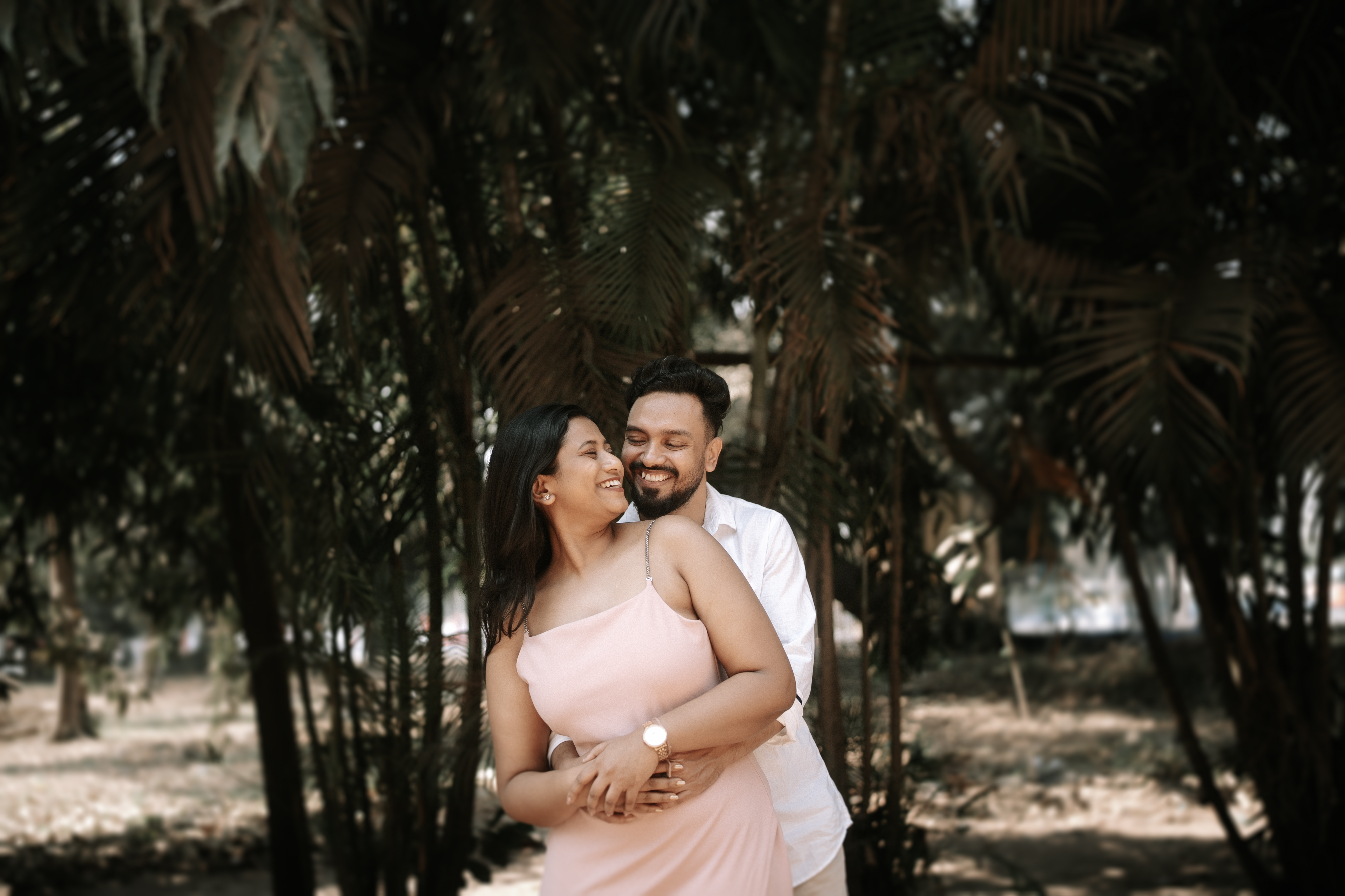 Rituparna and Shoumo embracing beneath a canopy of palm trees