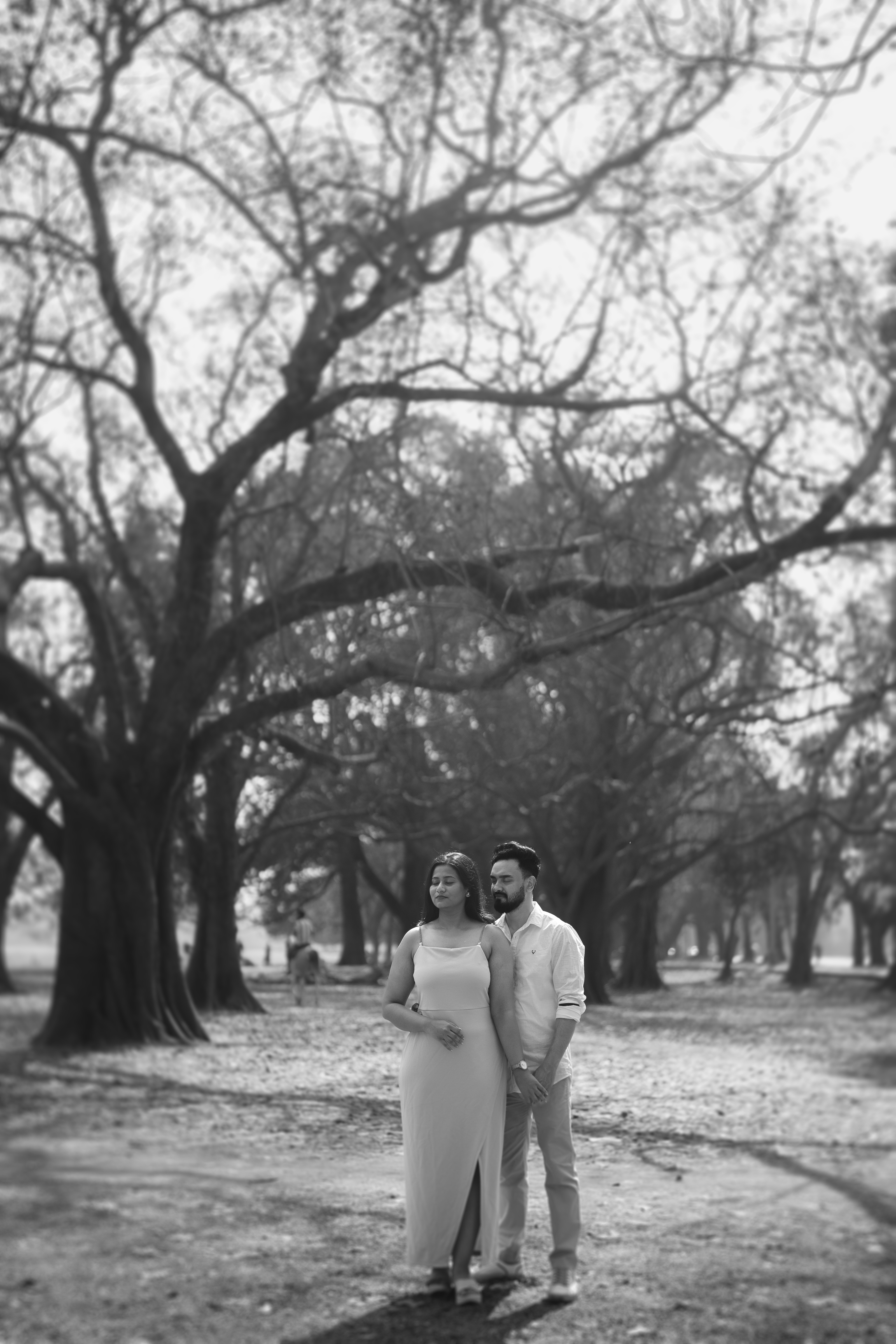 Black and white cinematic shot of the couple walking down a tree-lined avenue