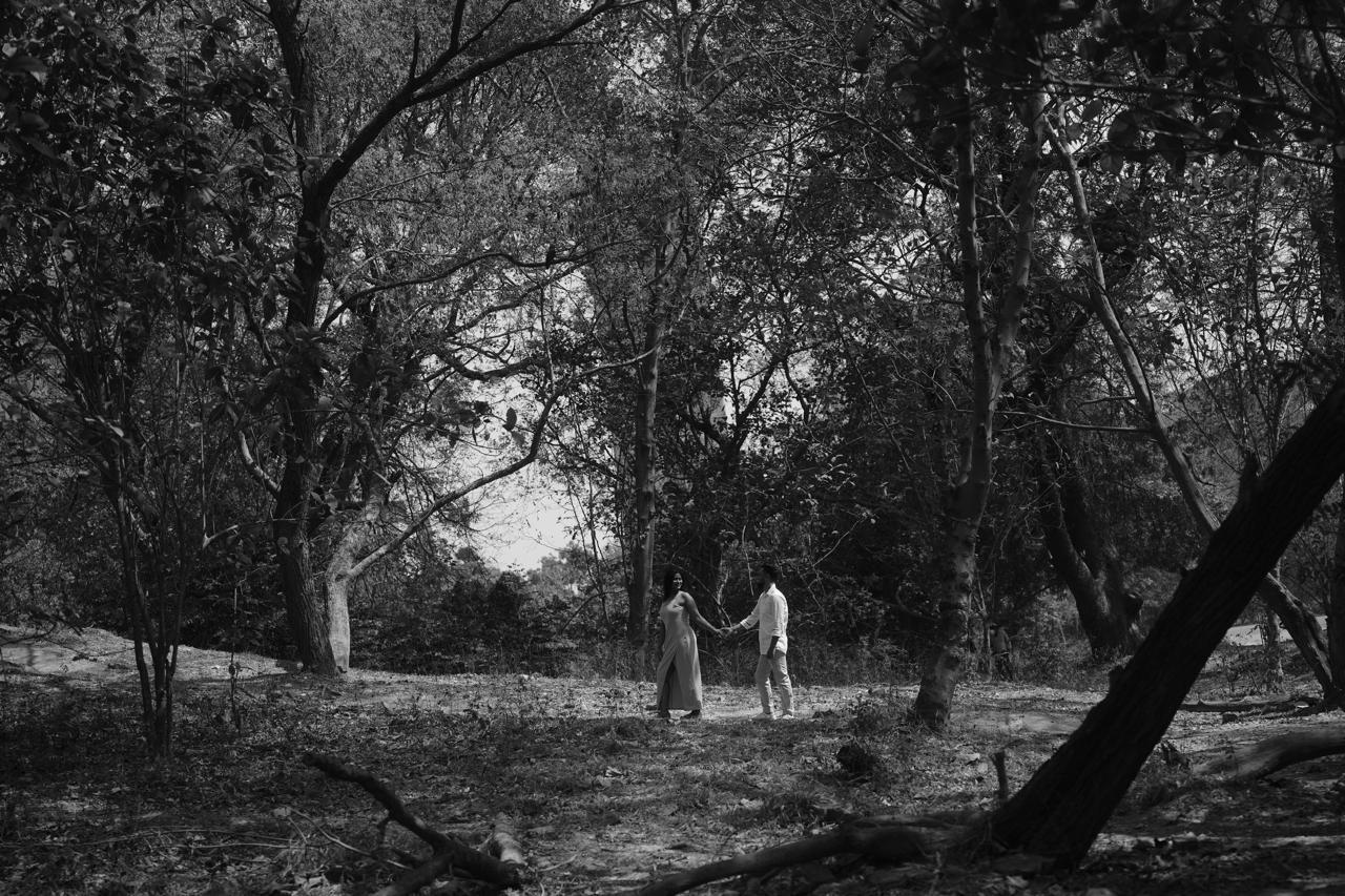 Black and white wide shot of the couple walking through a forest clearing