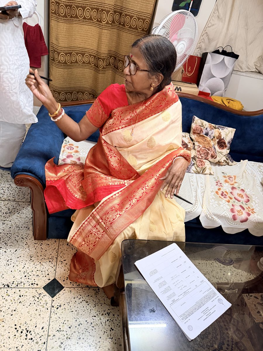 Elder woman in red and gold sari giving blessing with ceremonial items